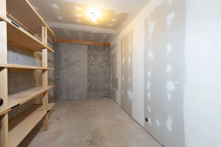 Unfinished room featuring built-in wooden shelving, concrete flooring, and exposed concrete walls
