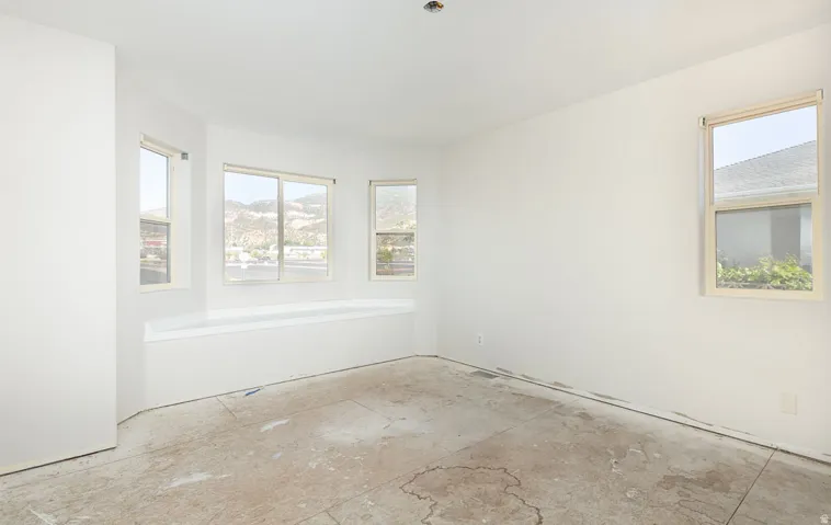 Spacious room featuring multiple windows, a built-in tub, bare concrete flooring, and white walls