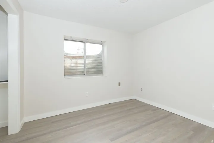 Room featuring light-toned wood-finish flooring, white baseboards, and a window with blinds