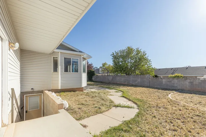 Expansive backyard featuring a curved concrete walkway, a full-height concrete block perimeter fence, and a sunroom extension