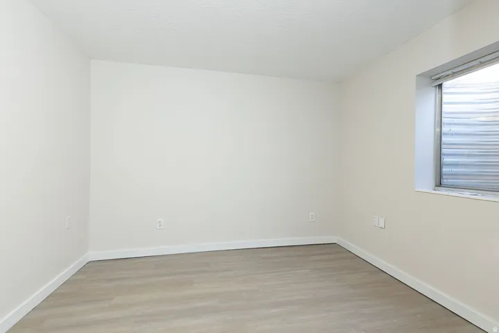 White-painted room featuring light wood-finish flooring, white baseboards, and a window with a corrugated metal window well