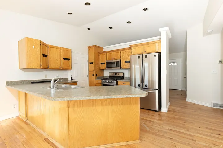 Kitchen featuring wood-finish cabinetry, stainless steel appliances, a center island with sink, recessed lighting, and wood-finish flooring