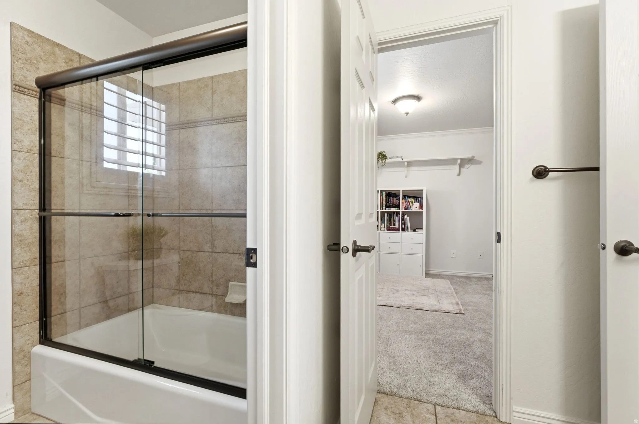Bathroom featuring a white bathtub with a bronze-framed glass shower enclosure, beige tiled walls, and a window with horizontal blinds