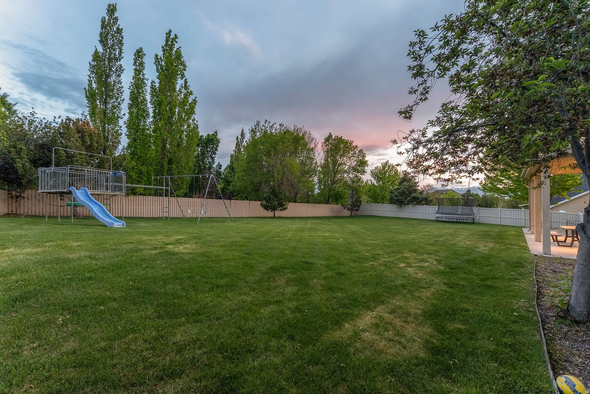 Expansive lawn featuring a privacy fence, mature trees, and a covered patio with built-in lighting