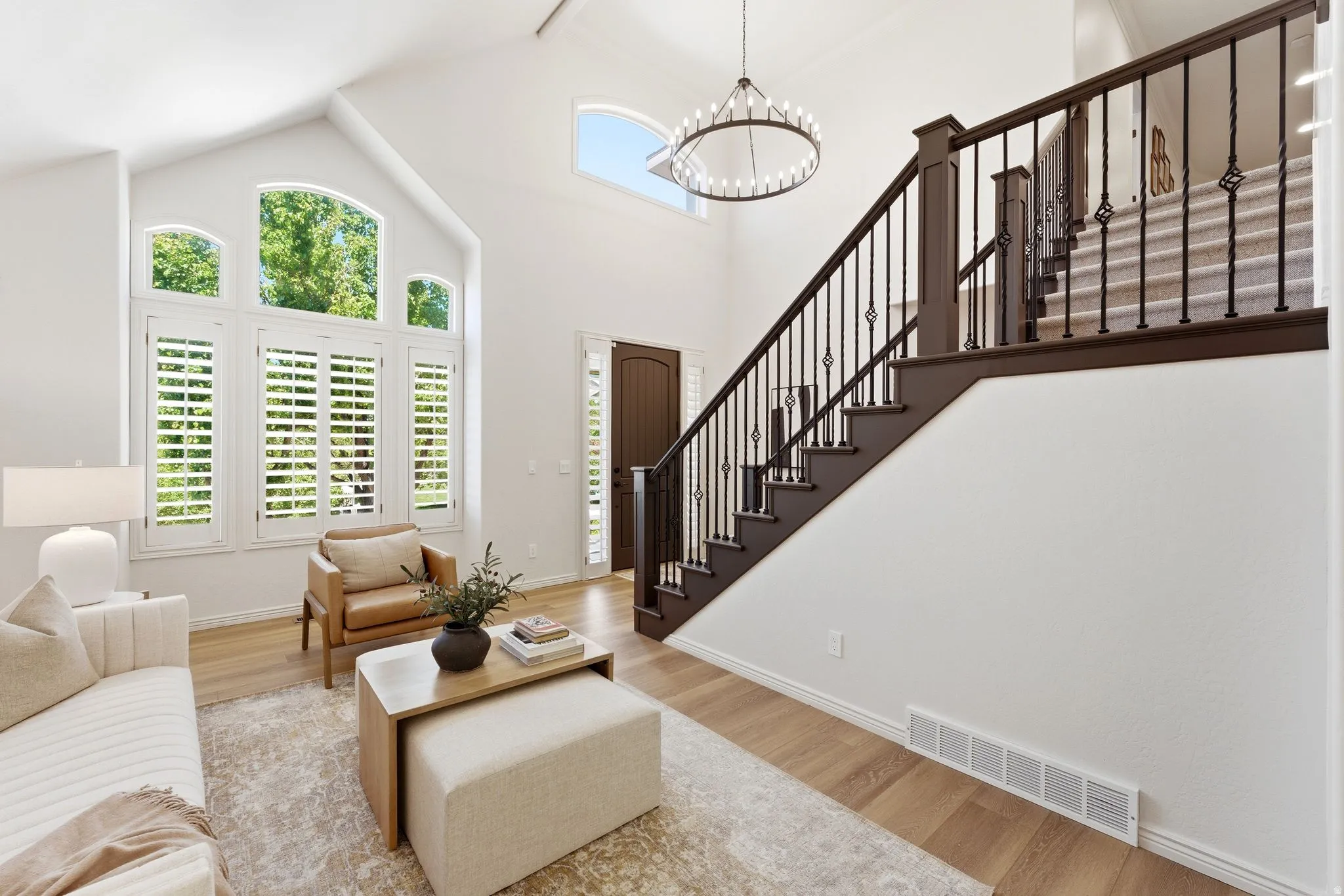 Two-story foyer featuring a wood-finish flooring, a grand staircase with wrought iron balusters, a decorative chandelier, and a prominent arched window with plantation shutters
