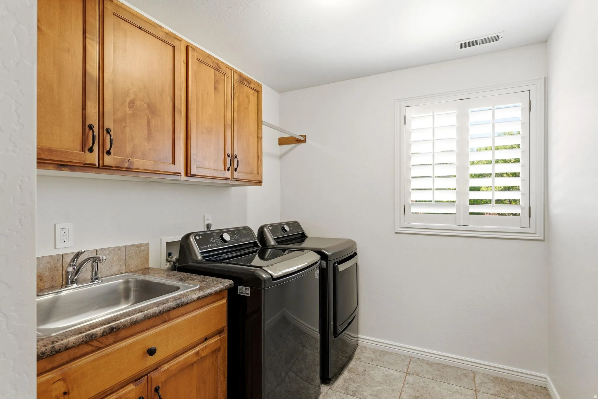 Dedicated utility space featuring light wood cabinetry, a built-in sink with a chrome faucet, and a stone-finish countertop