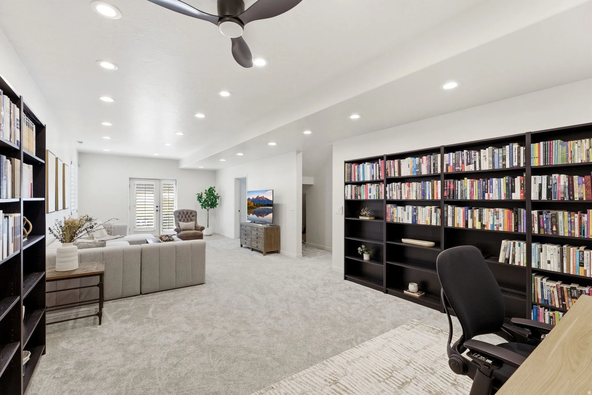 Spacious room with built-in dark wood-finish bookcases, recessed lighting, and light gray carpet flooring