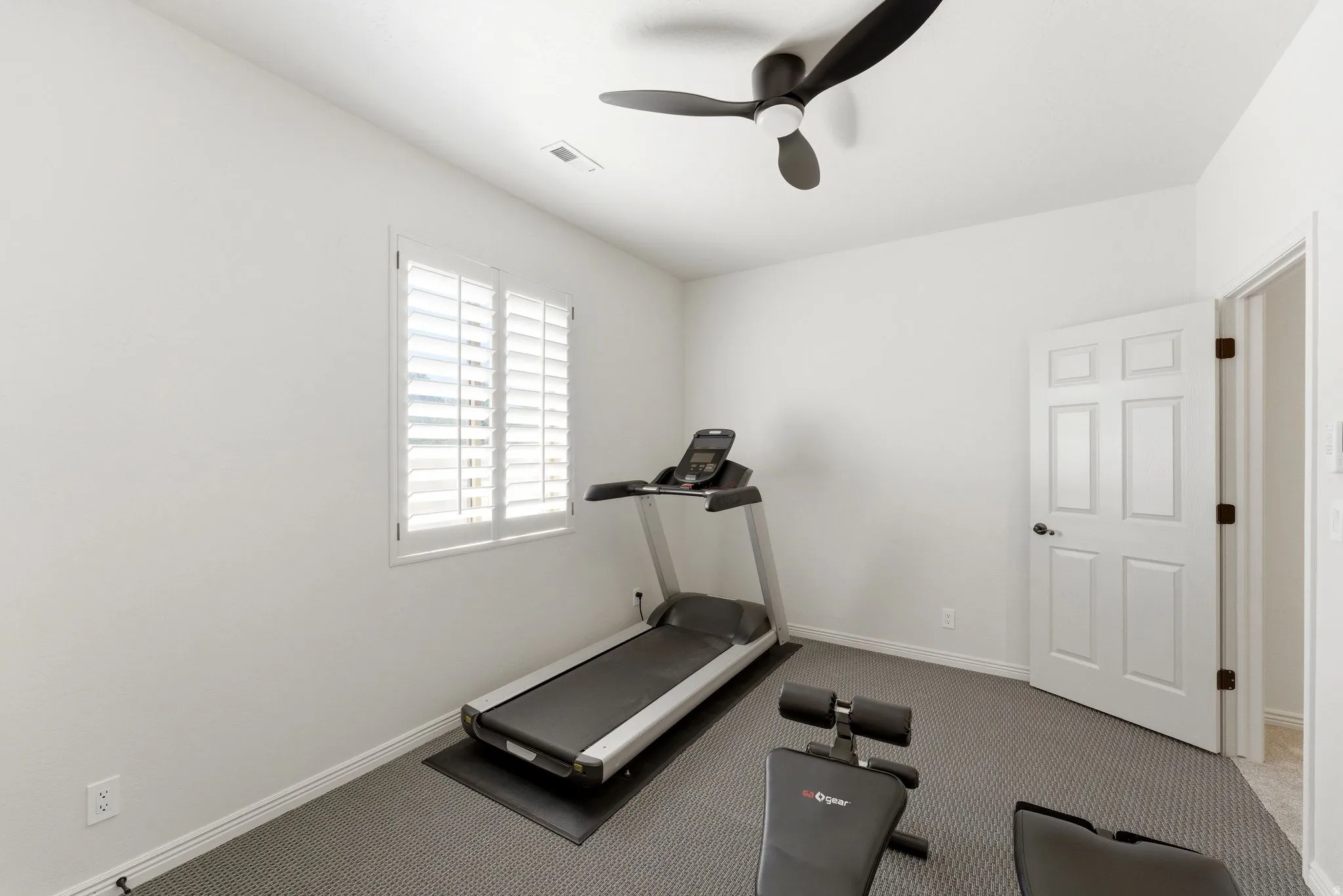 Interior room featuring white walls, a single window with white plantation shutters, and a dark ceiling fan with three blades