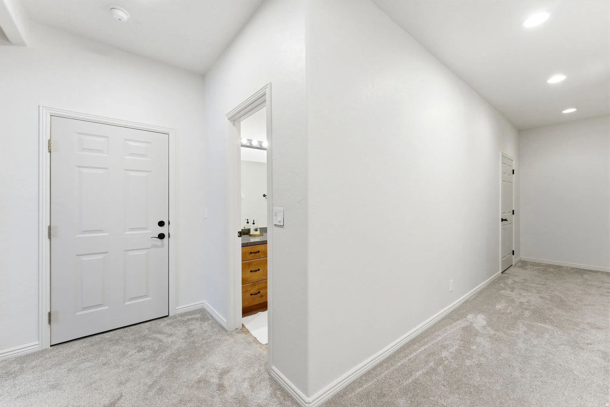 Hallway with light gray carpeting, white baseboards, and bright white walls