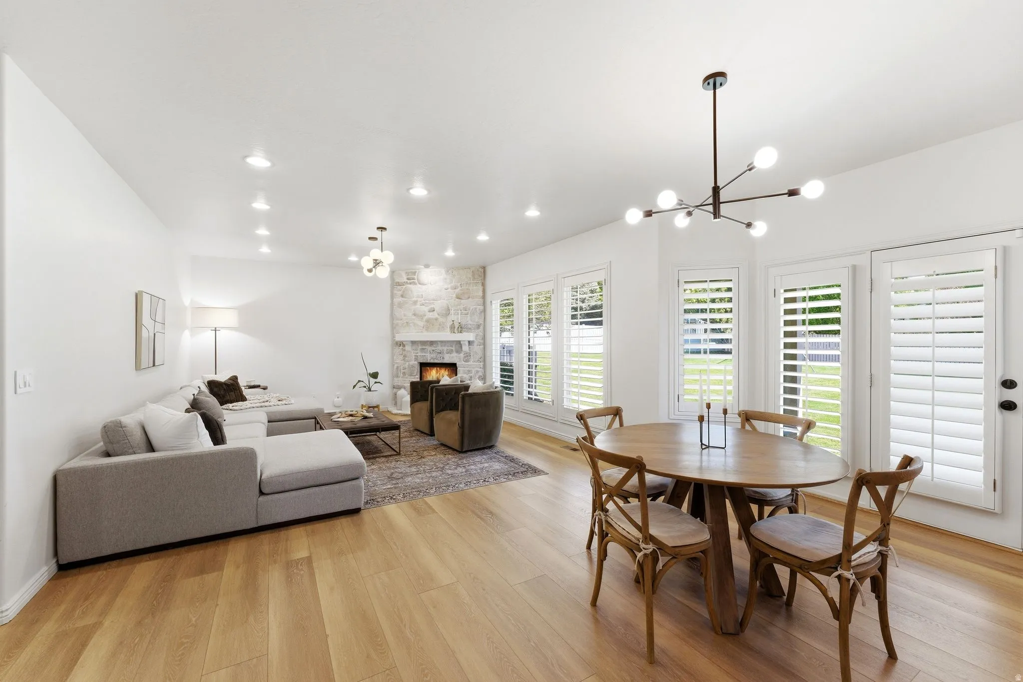 Open-concept living area featuring wood-finish flooring, a stone-surround fireplace, and recessed lighting throughout