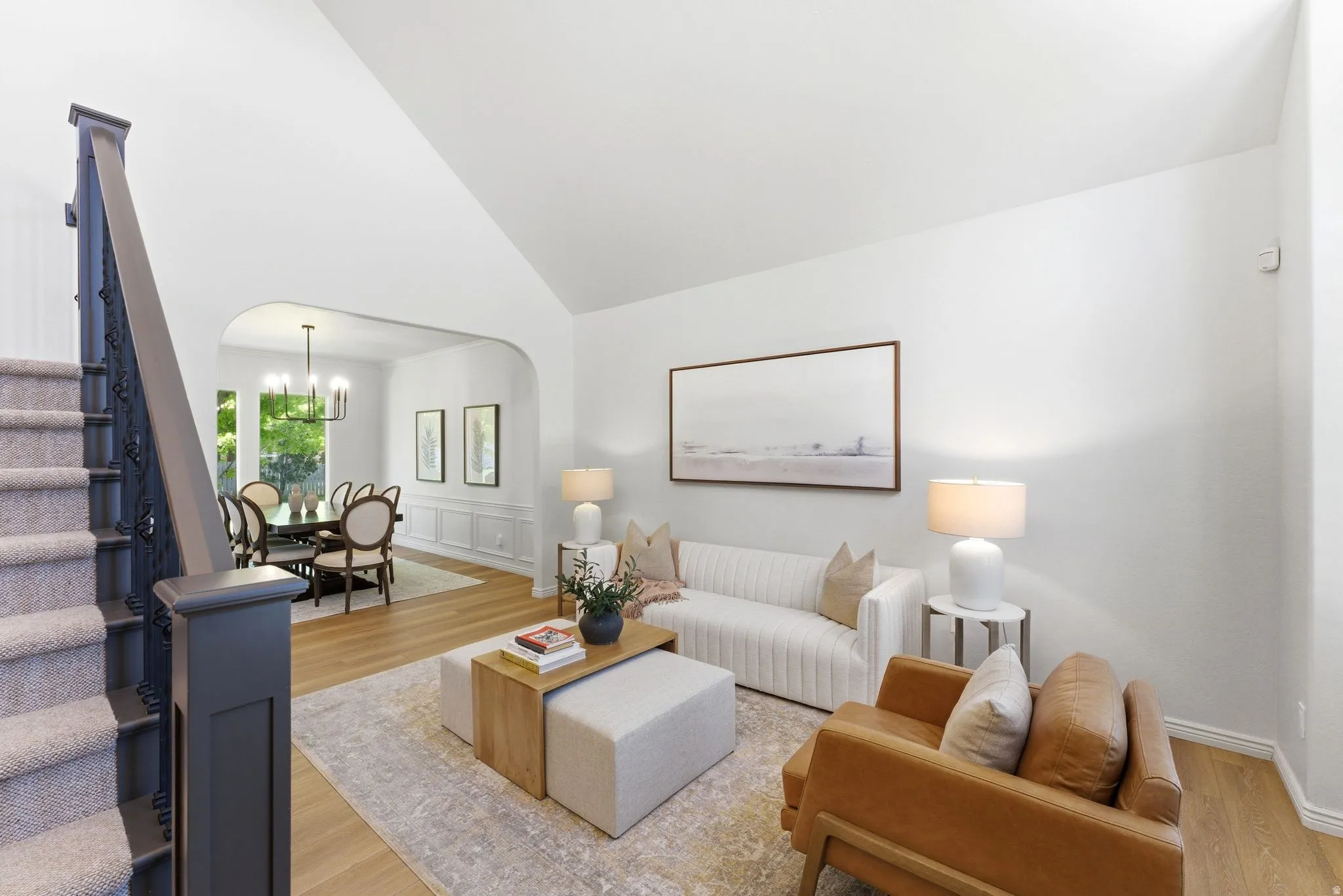Living area with wood-finish flooring, vaulted ceiling, and an arched entry to a dining space