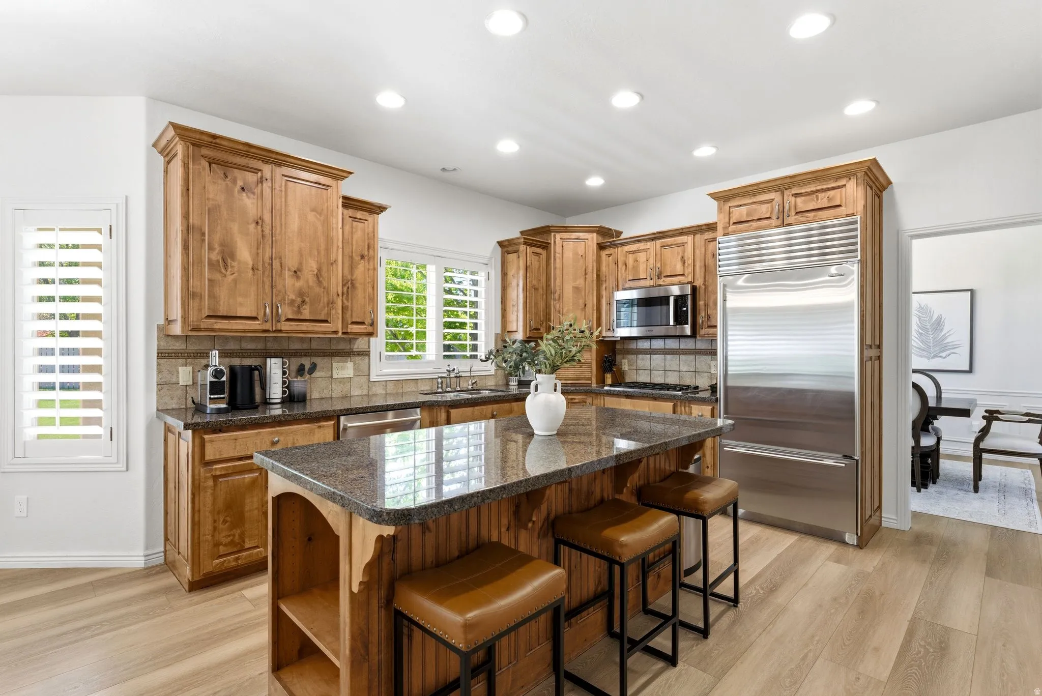 Kitchen featuring wood-finish cabinetry, stainless steel appliances, an island with a stone countertop, recessed lighting, and wood-finish flooring