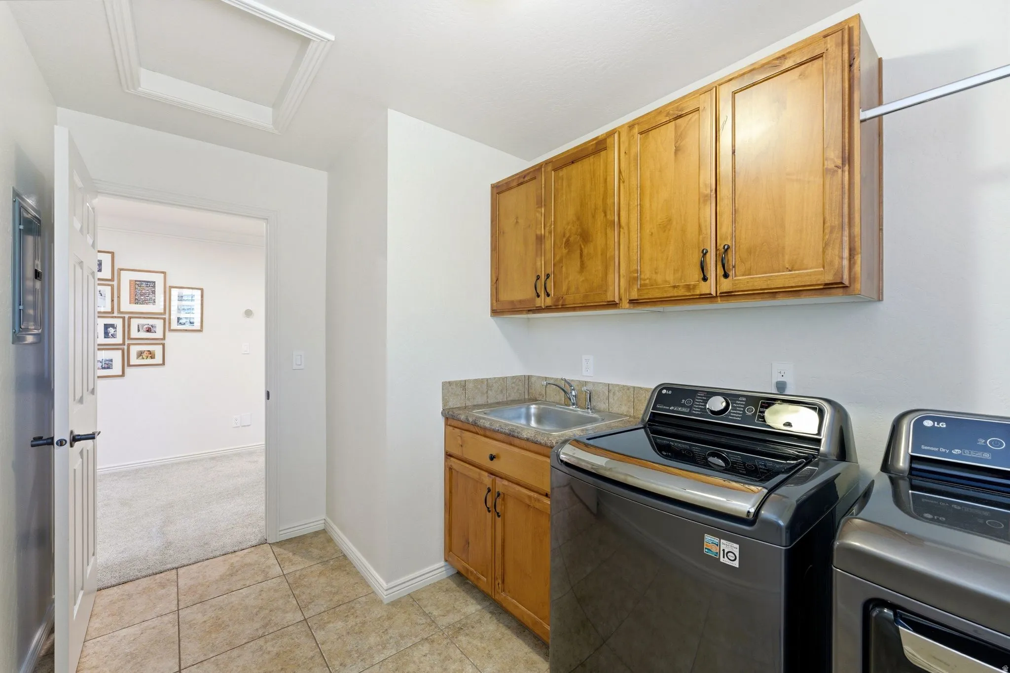 Laundry area featuring tile flooring, wood-finish cabinetry, a utility sink, and a hanging rod
