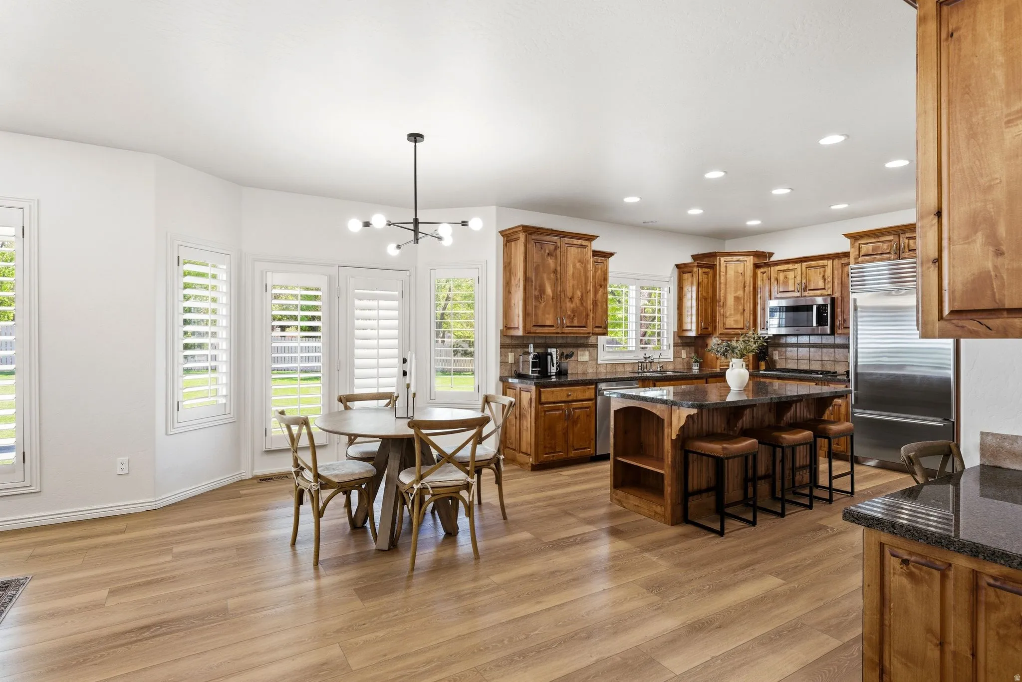 Open-concept kitchen and dining area featuring wood-finish flooring, recessed lighting, and a modern chandelier