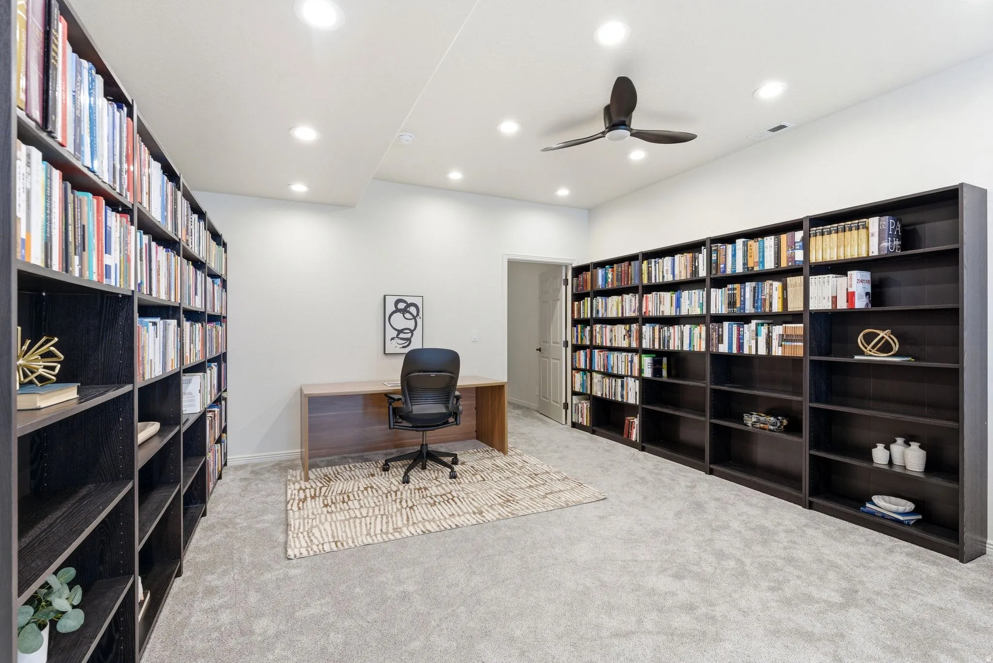 Dedicated office space featuring extensive built-in shelving, recessed lighting, and a ceiling fan