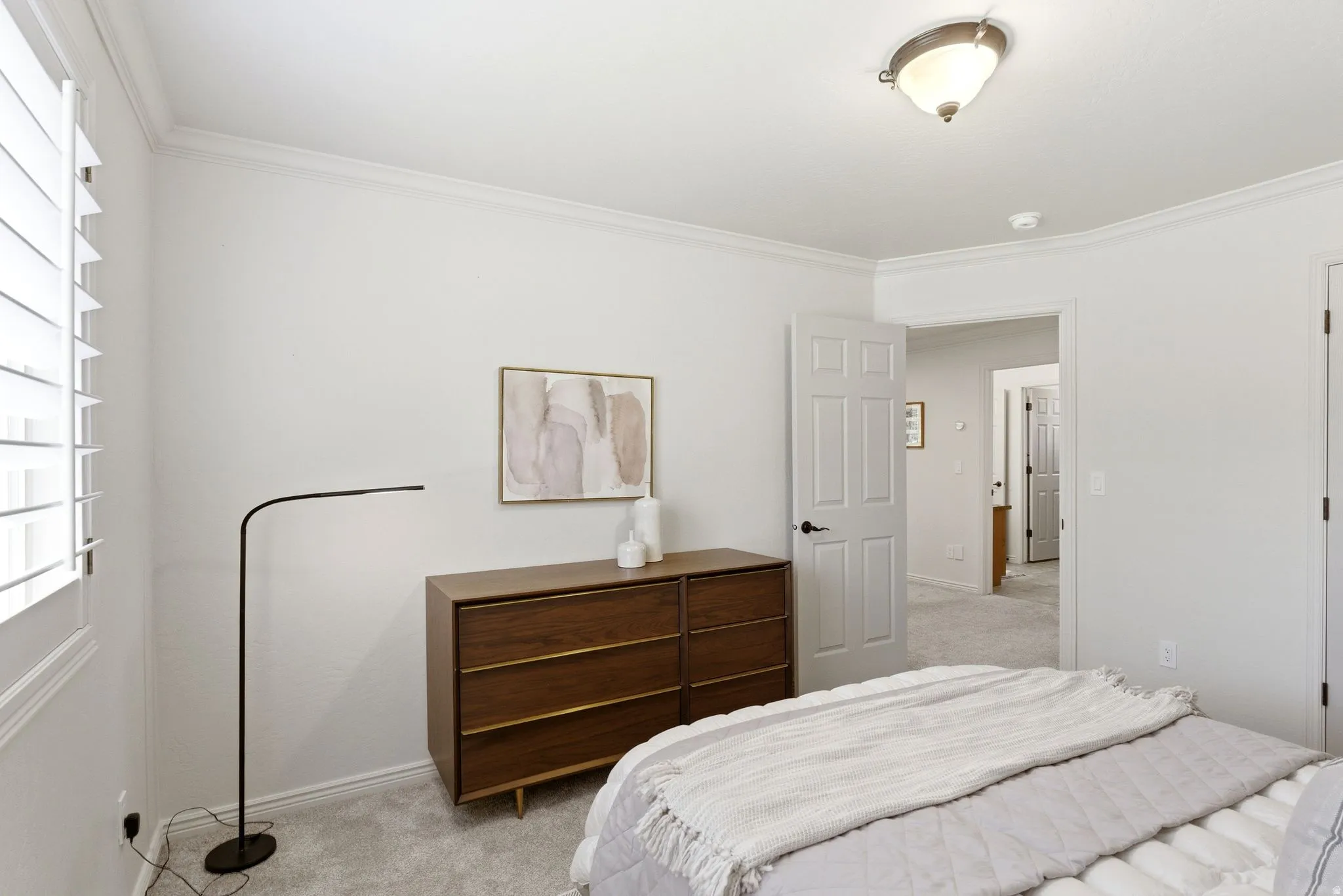Bedroom featuring white interior walls, white crown molding, white plantation shutters, and light gray carpet flooring