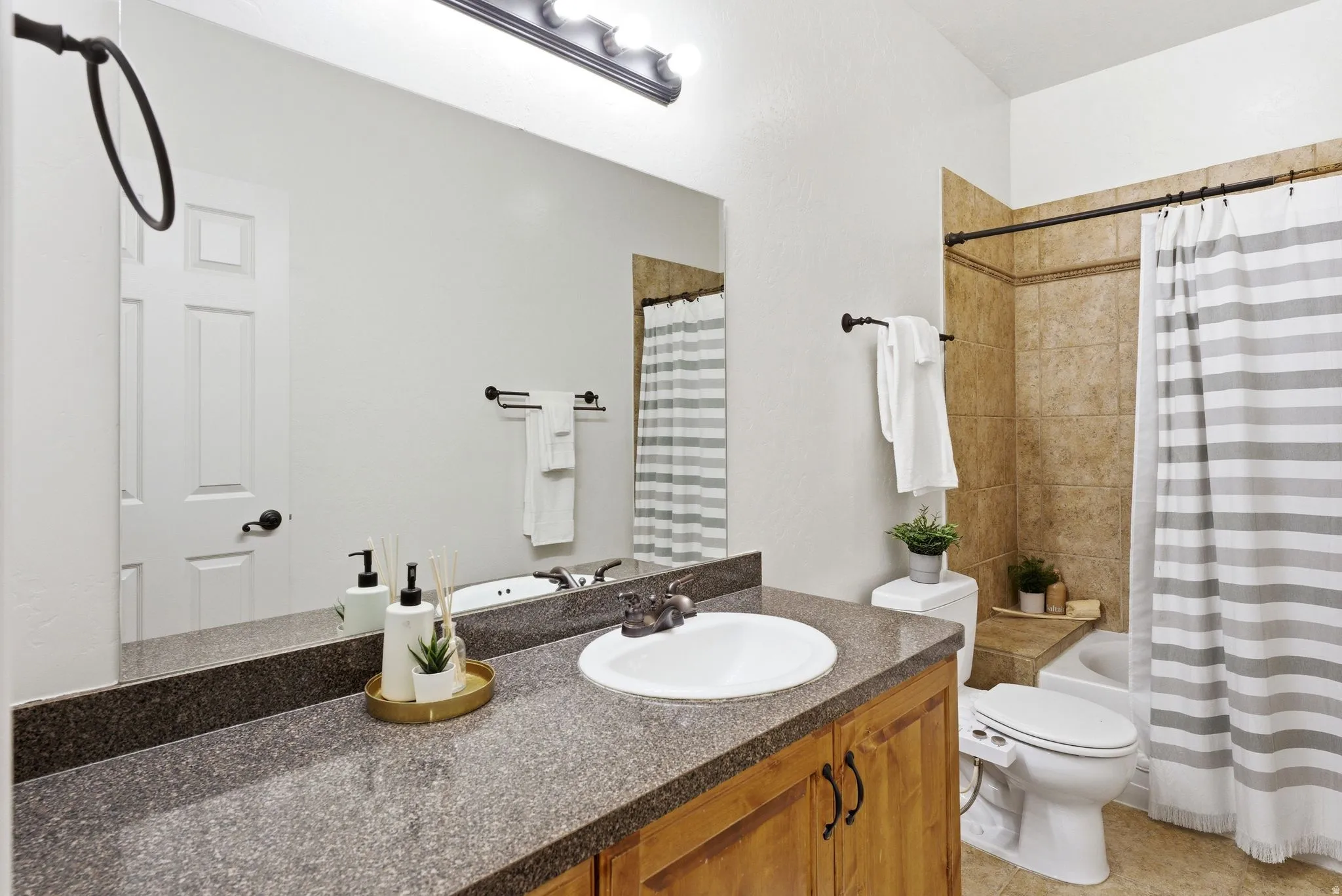 Full bathroom featuring a wood-finish vanity with a speckled countertop, a large integrated mirror, and a ceramic sink