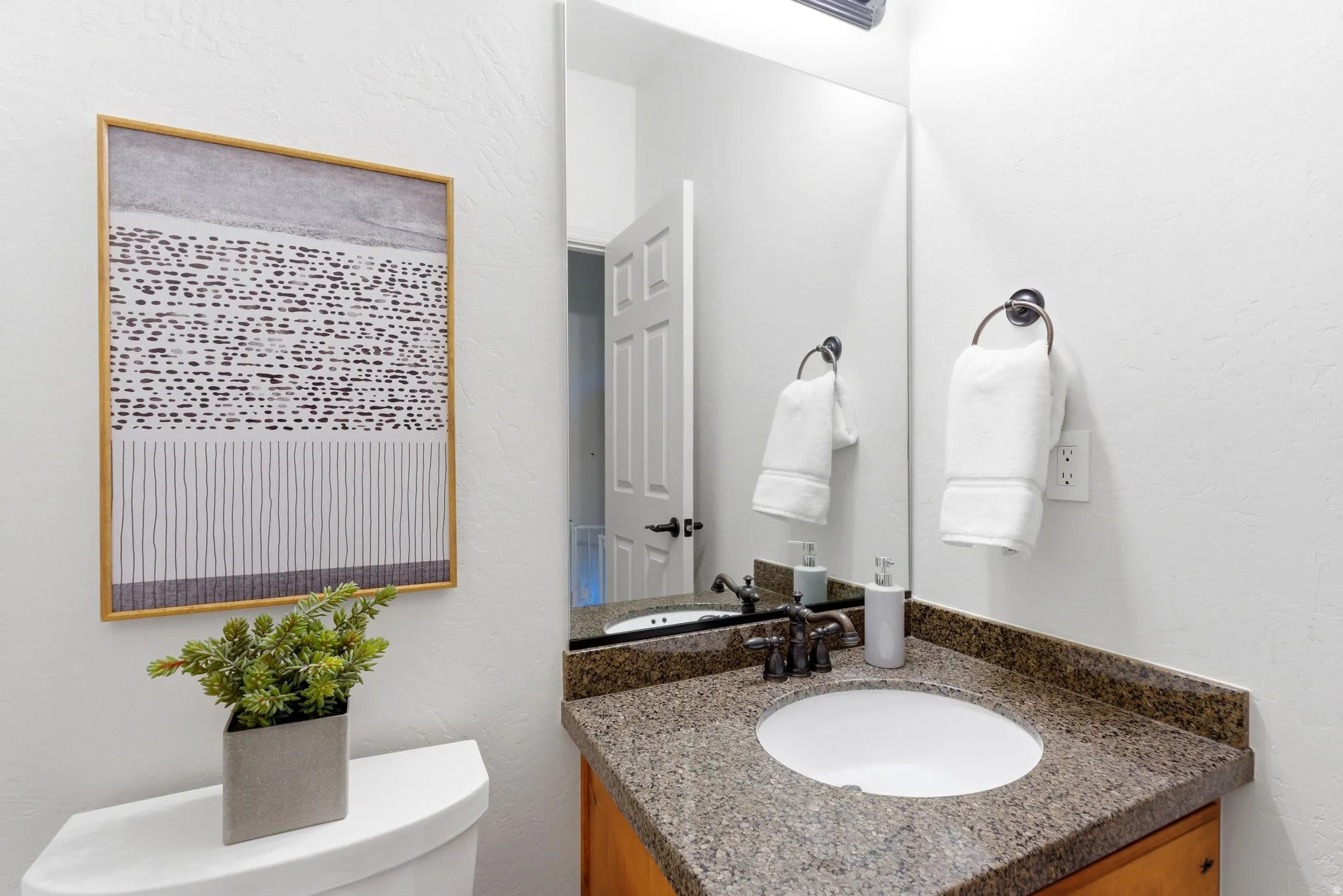 Powder room featuring a granite countertop, undermount sink, bronze-finish faucet, framed mirror, and light wood-finish cabinetry