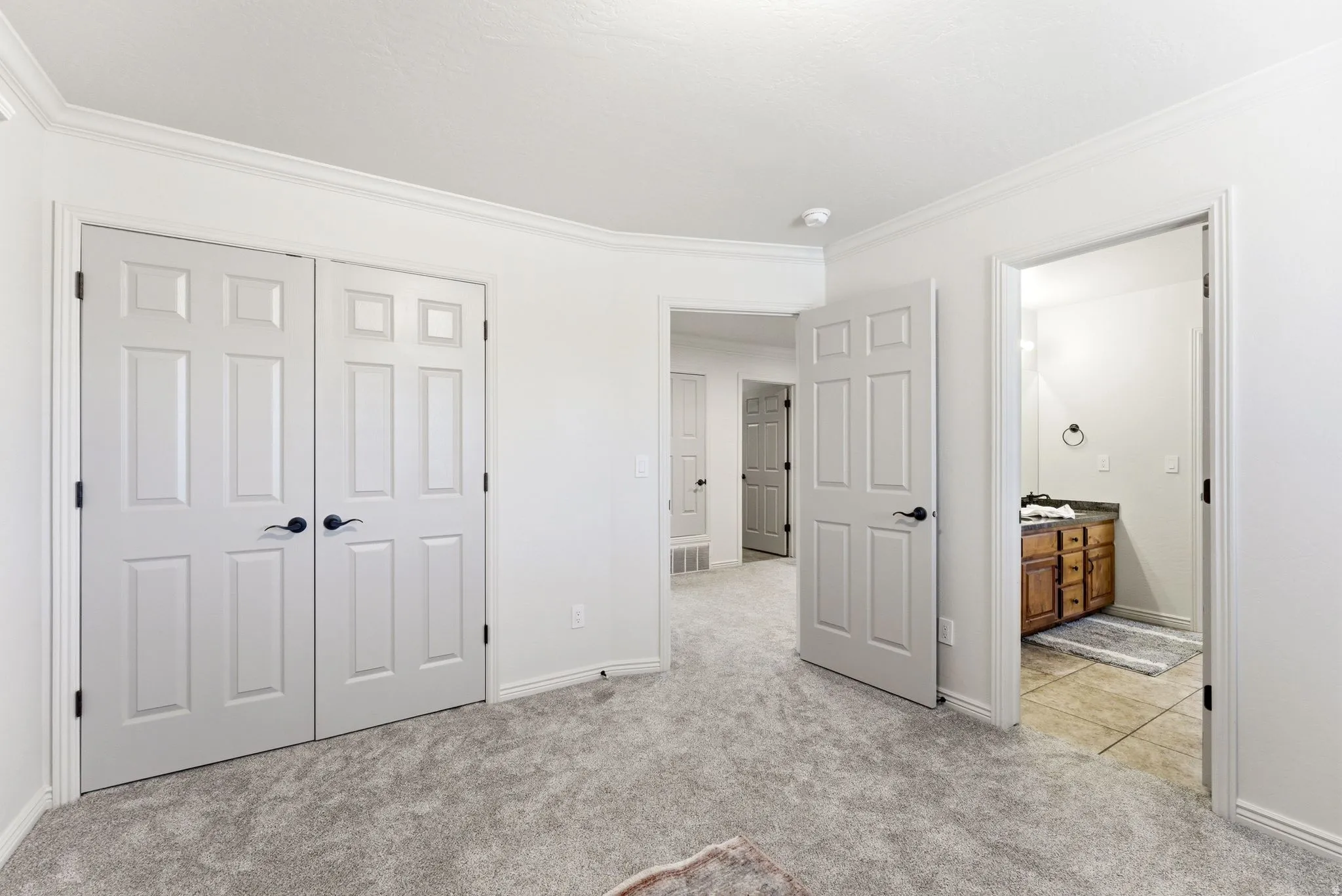 Carpeted room featuring white paneled double doors with black hardware, white baseboards, and crown molding