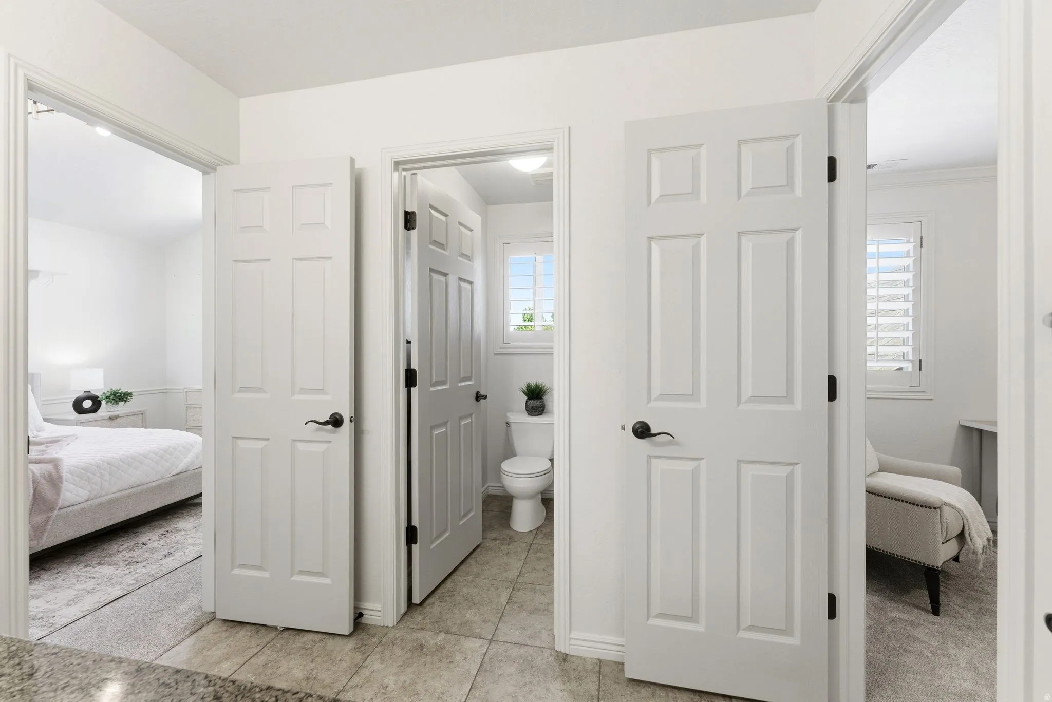 White paneled interior doors with black hardware, tile flooring, and light-filled rooms with white walls and window shutters