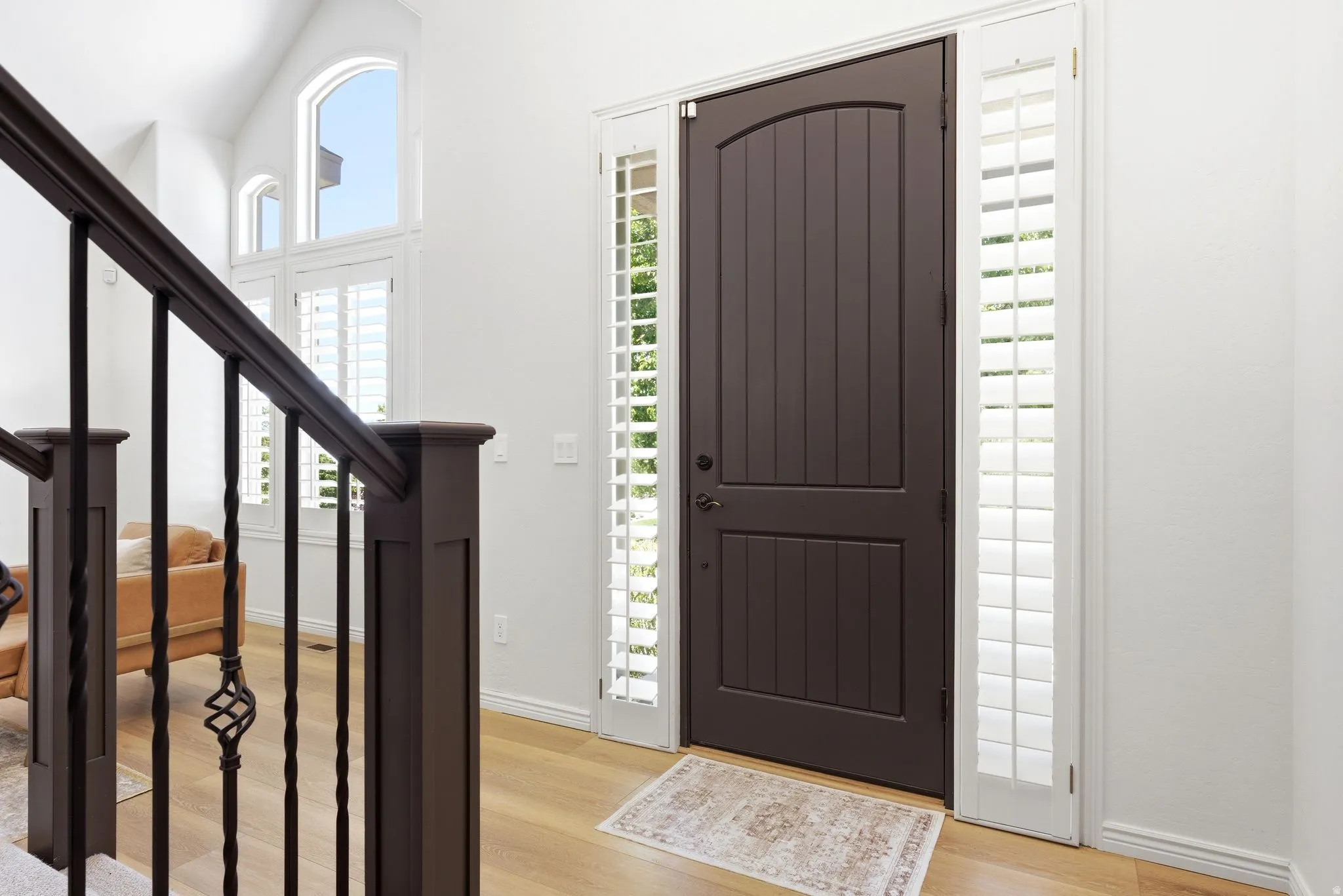 Entryway featuring a dark wood-finish arched door, flanking sidelights with plantation shutters, and wood-finish flooring