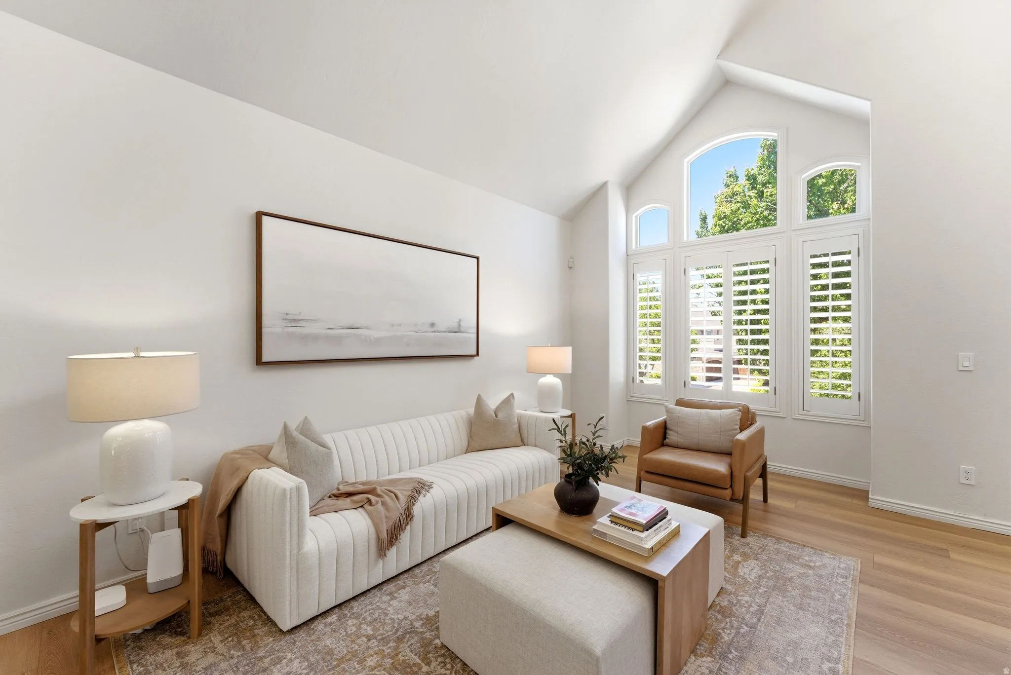 Vaulted ceiling living space featuring a wall of plantation-shuttered windows, arched transom windows, wood-finish flooring, and crisp white walls