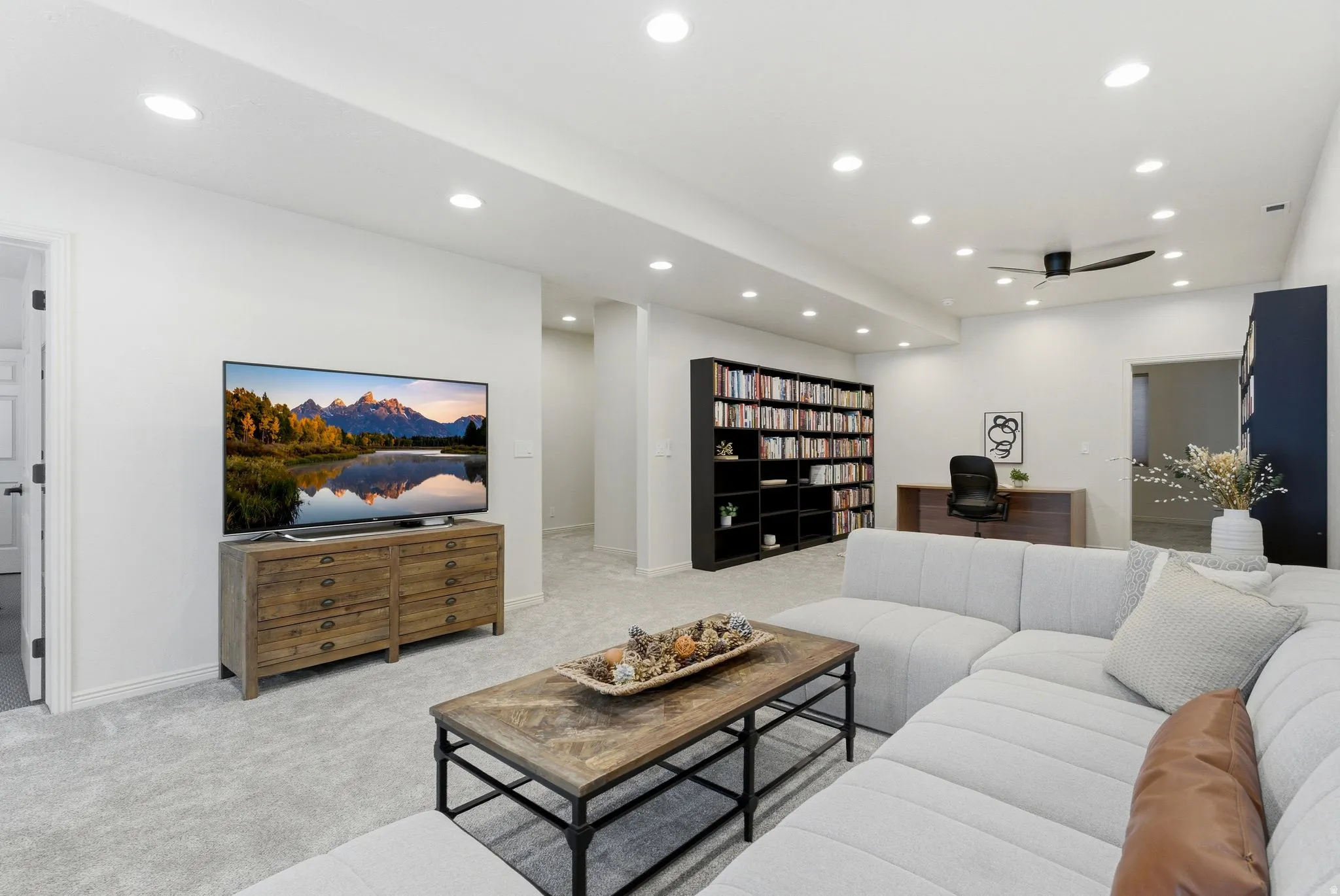 Spacious open-concept room featuring light-toned carpeting, ample recessed lighting, and a modern ceiling fan