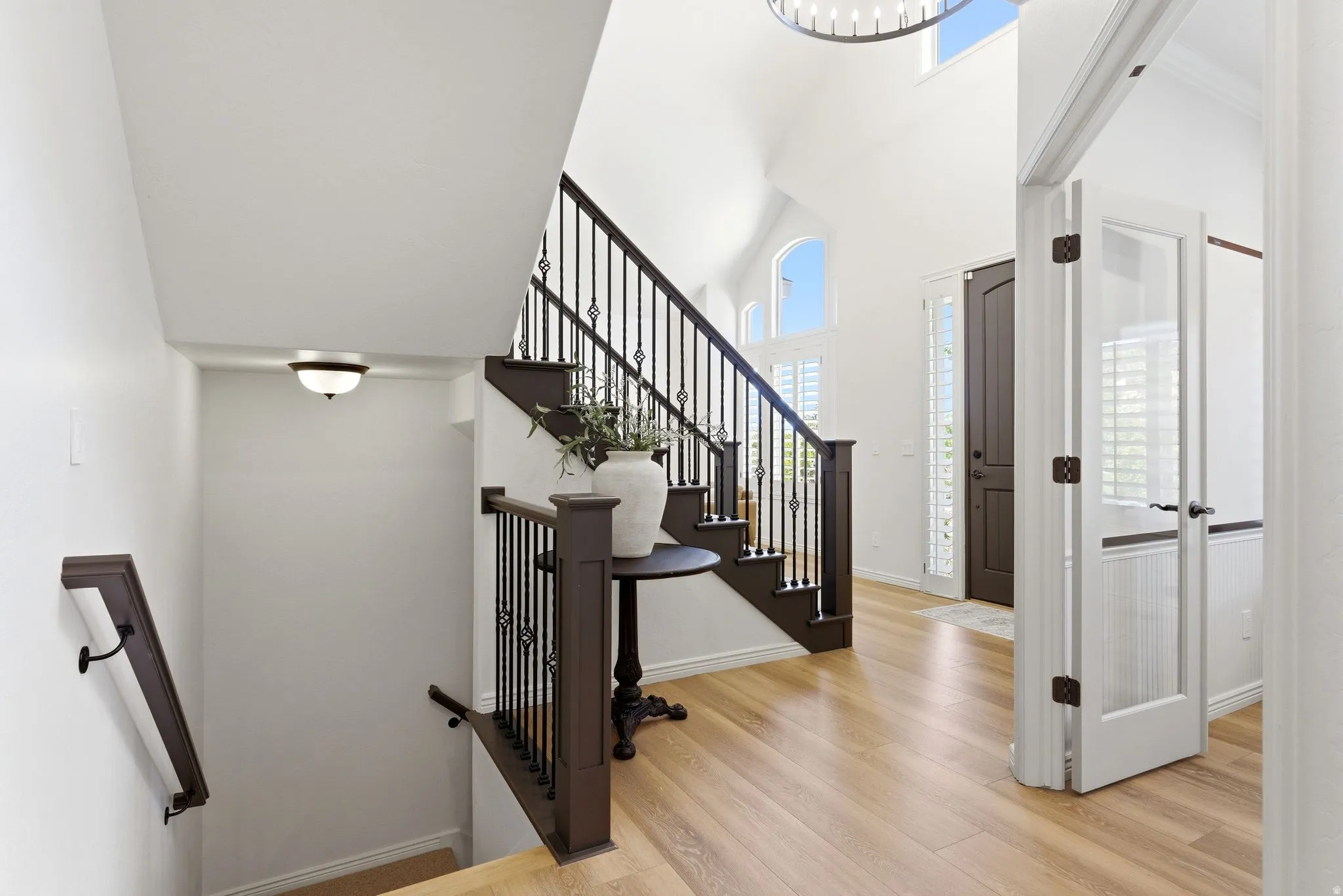 Two-story foyer featuring high vaulted ceilings, light wood-finish flooring, and a dark wood staircase with wrought iron balusters