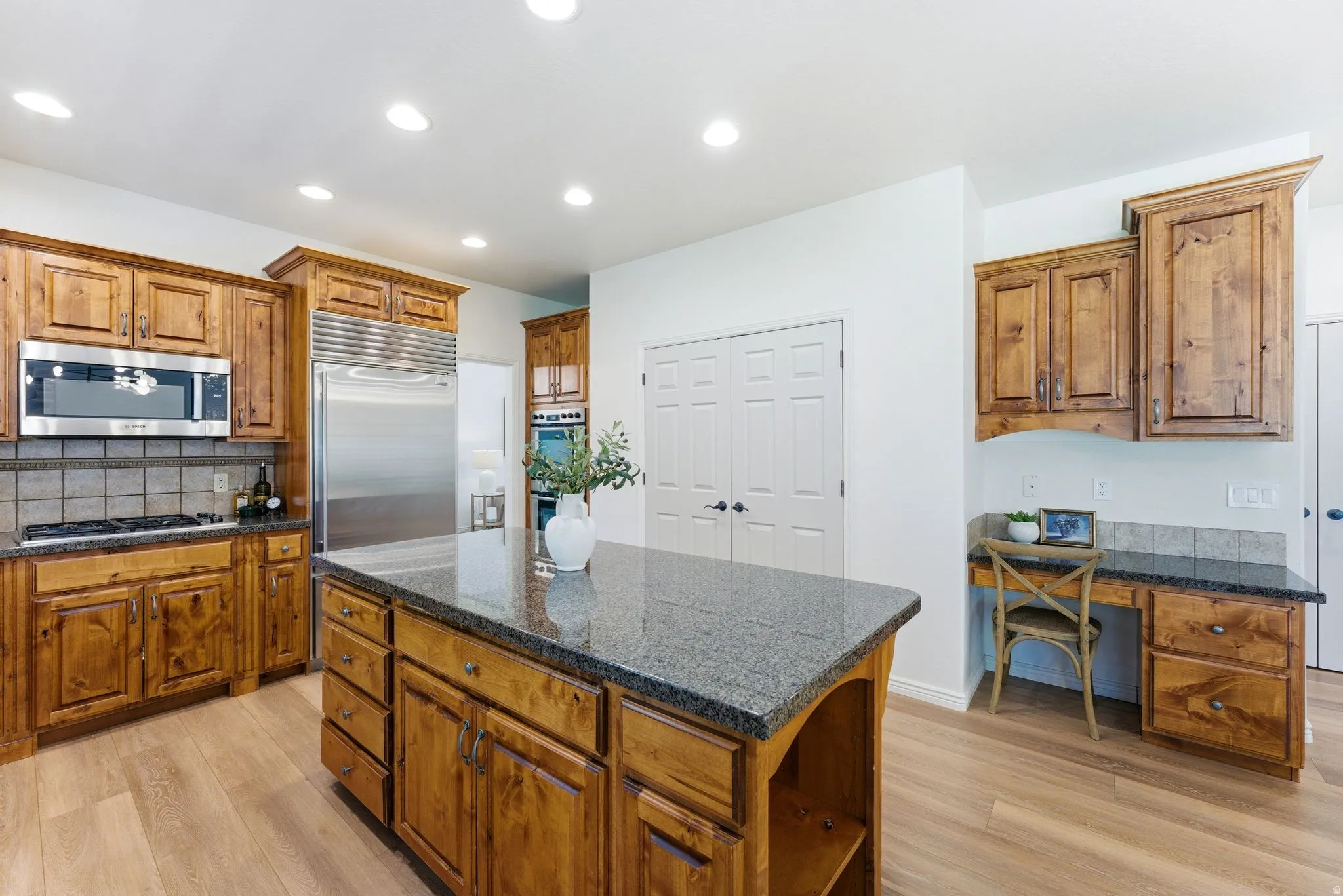 Kitchen featuring a large island with a stone countertop, wood-finish flooring, stainless steel appliances, recessed lighting, and ample wood cabinetry
