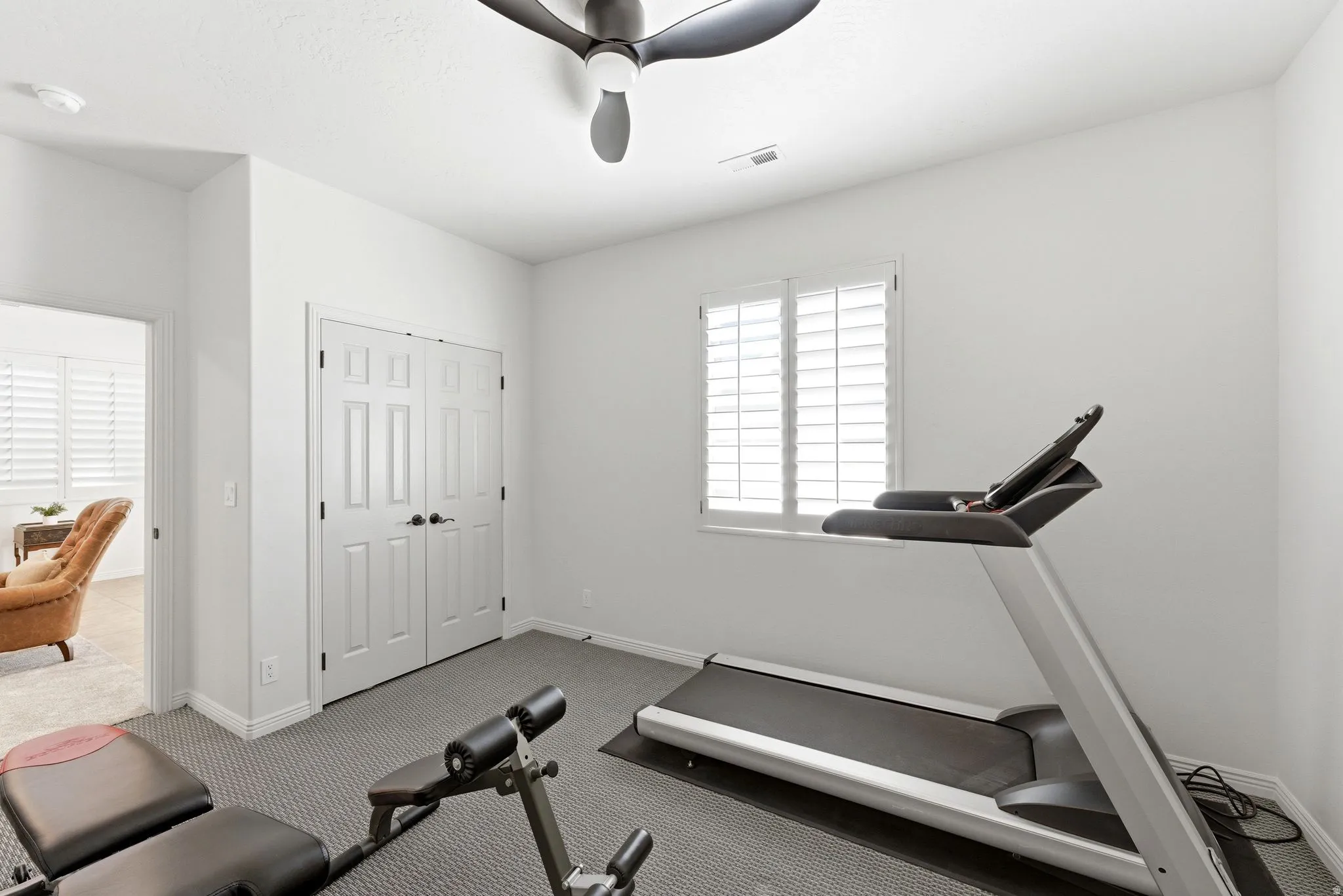 Room featuring a multi-panel window with plantation shutters, a ceiling fan, and double panel doors with dark hardware