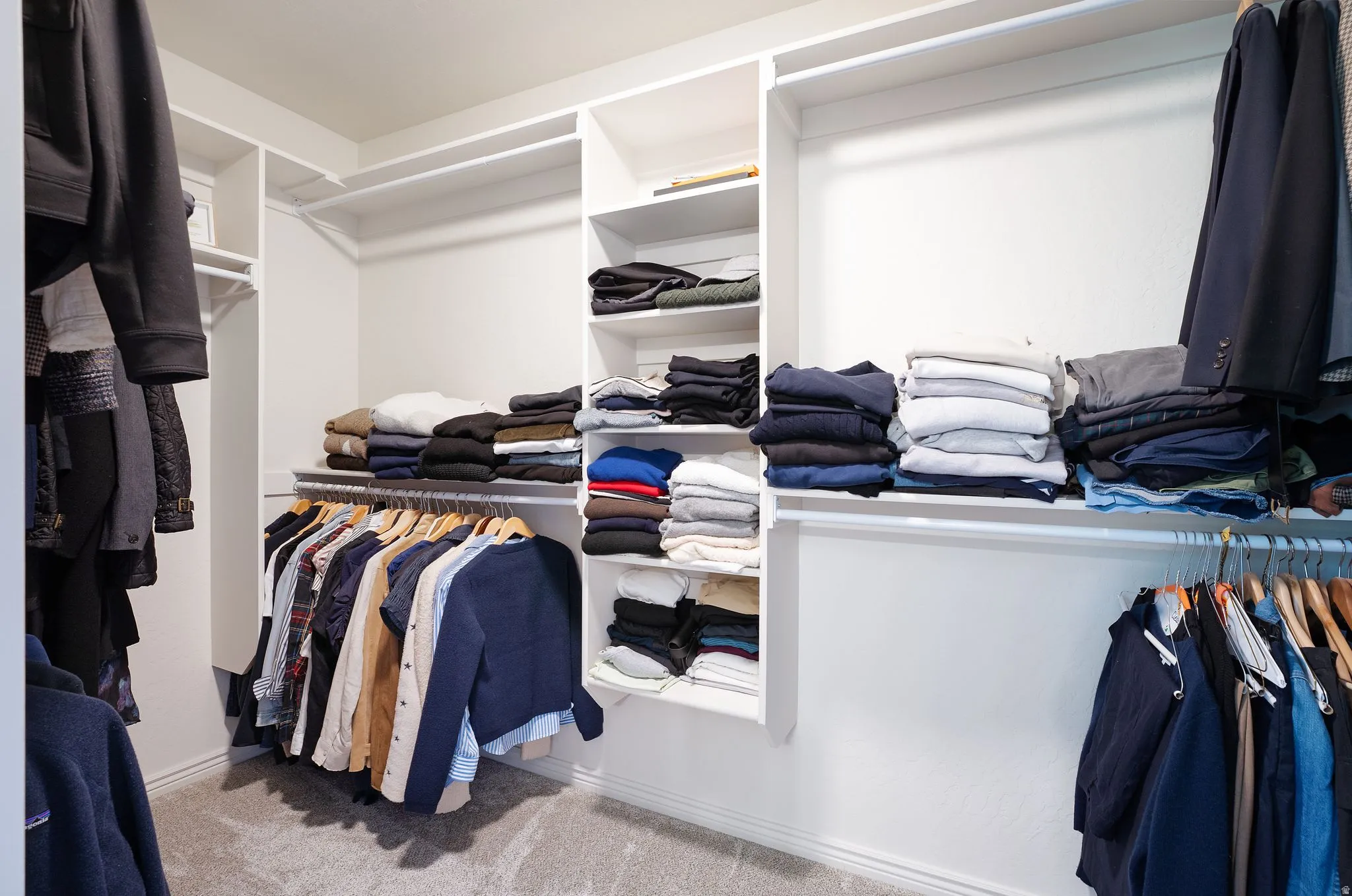 Custom white built-in closet system with multiple shelving units and hanging rods, set against light-colored walls, with a gray carpeted floor