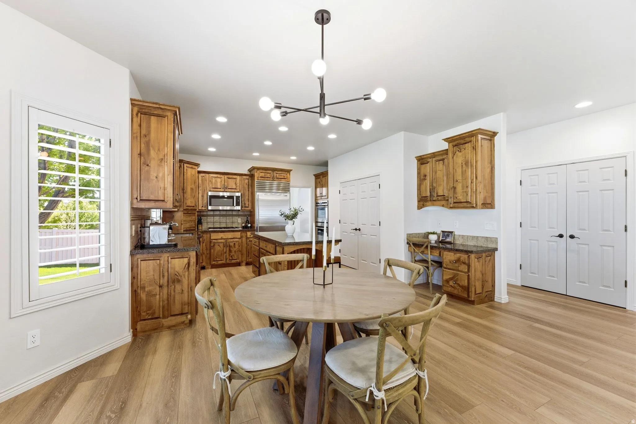 Spacious kitchen and dining area featuring light wood-finish flooring, recessed lighting, and a modern chandelier