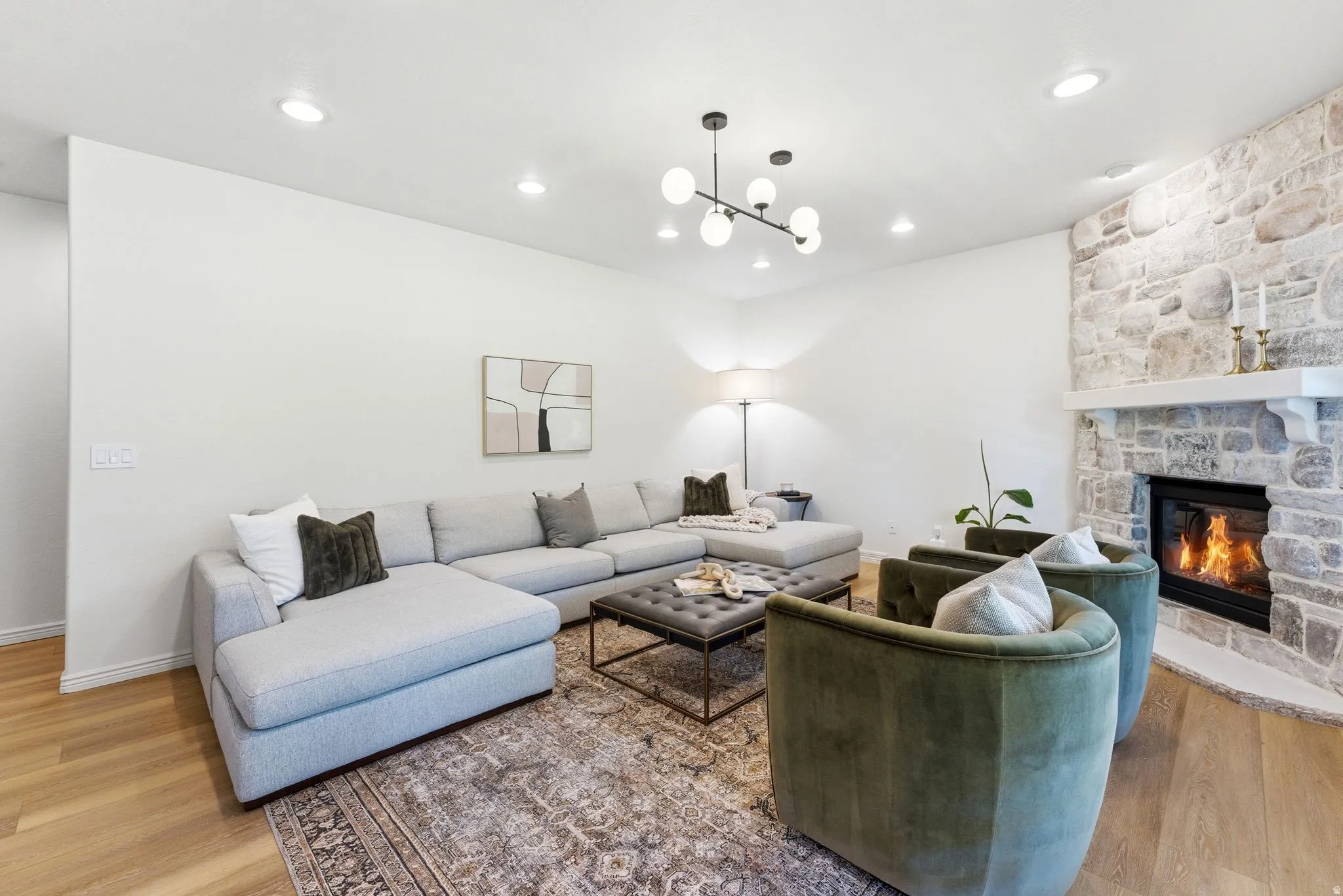 Spacious living area featuring a stone fireplace with a substantial mantel, wood-finish flooring, recessed lighting, and a contemporary spherical chandelier