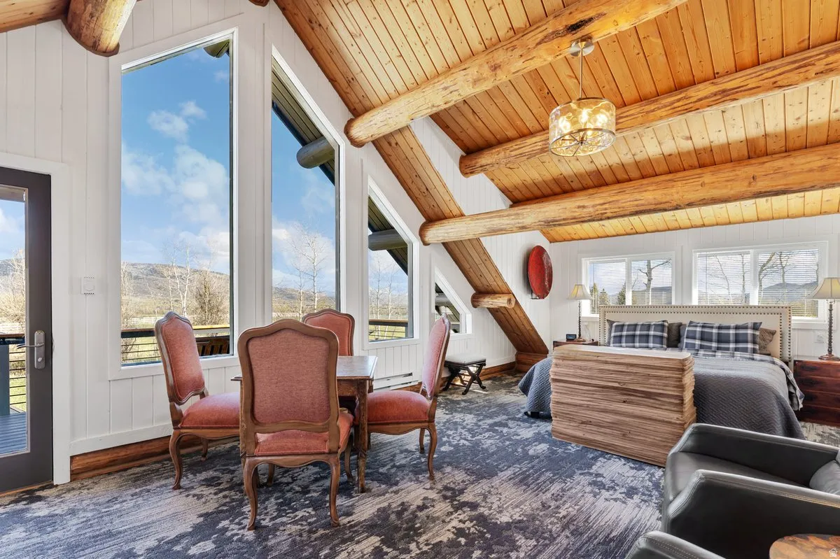 Vaulted wood-plank ceilings featuring exposed log beams, extensive wall-to-wall windows, and a glass-paneled exterior door