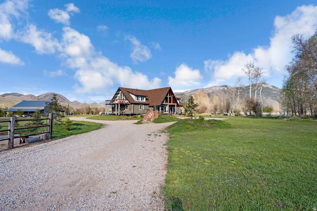 Expansive gravel driveway leading to a multi-level residence with a distinct brown shingle roof and a raised deck