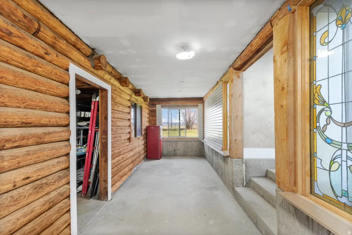 Rustic log wall construction with exposed beams, concrete flooring, and a decorative stained-glass window