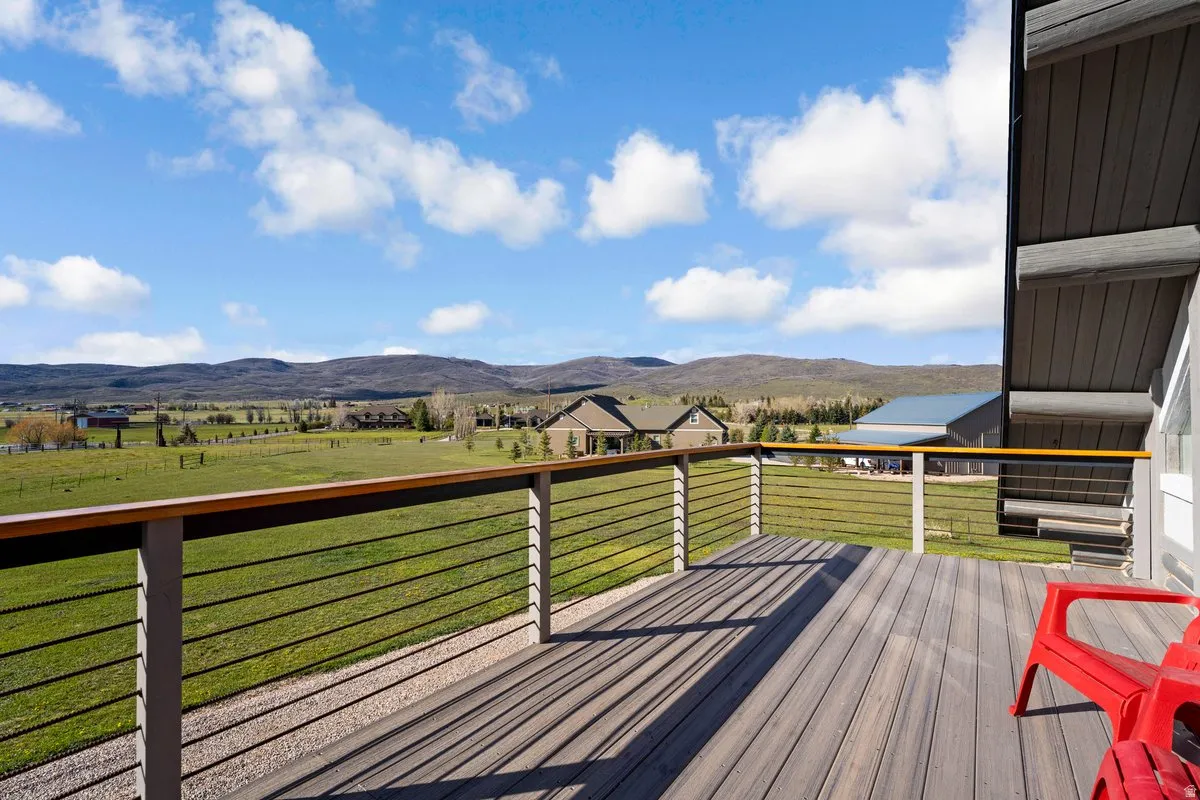 Spacious outdoor deck featuring composite decking, a cable railing system with wood-finish top rail, and an expansive rural landscape with distant mountains