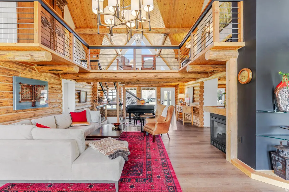 Spacious living area featuring exposed log walls, high vaulted ceilings with wood paneling, wood-finish flooring, a built-in fireplace, and an open loft area with metal railings