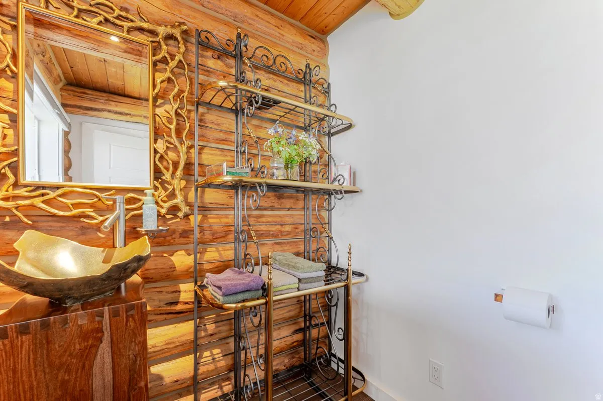 Rustic wood paneling and log ceiling details complemented by a unique gold-toned vessel sink and a custom mirror with a branch-like frame