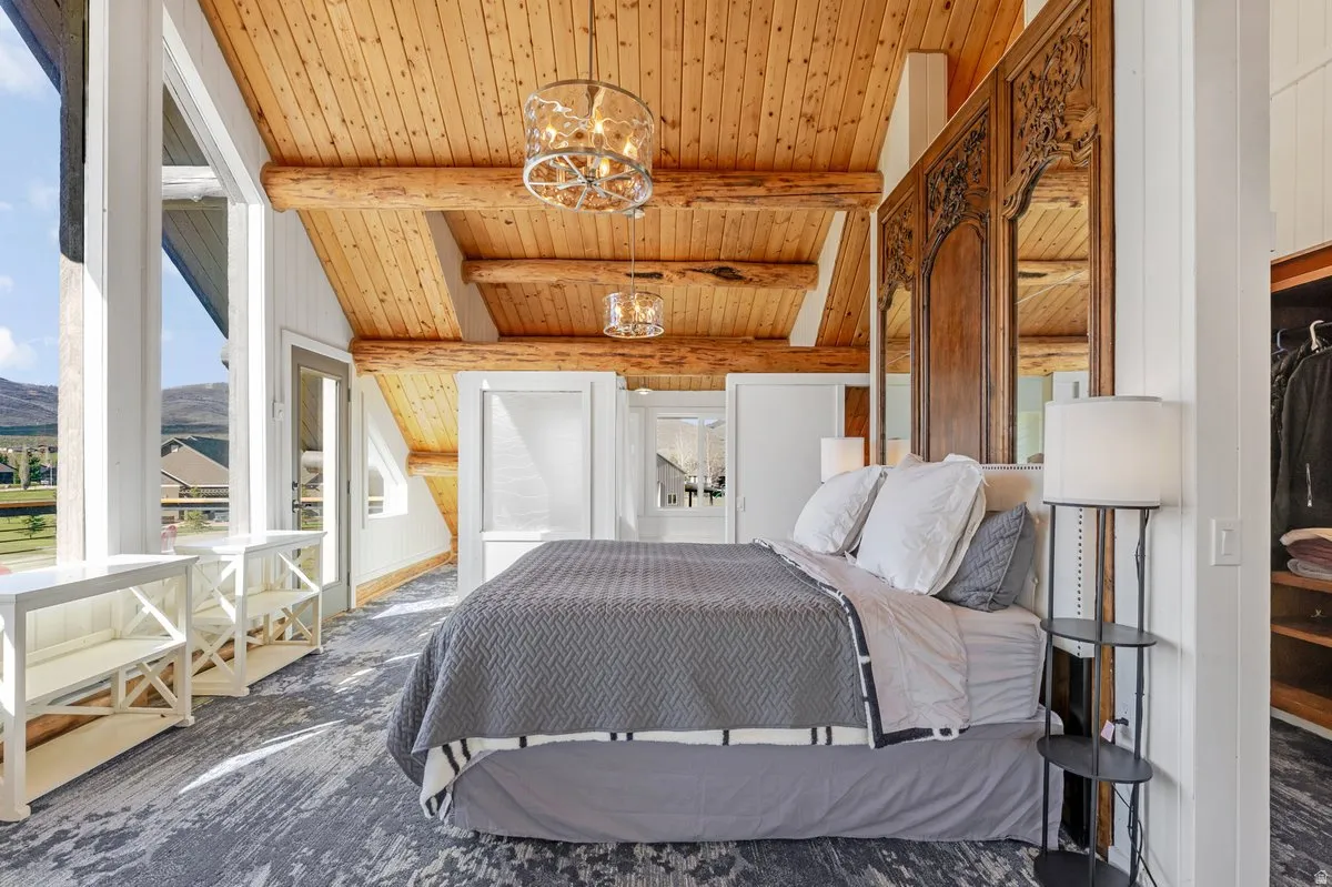 Room featuring an exposed wood plank ceiling with log beams, a carved wood headboard, and a walk-in closet with built-in shelving