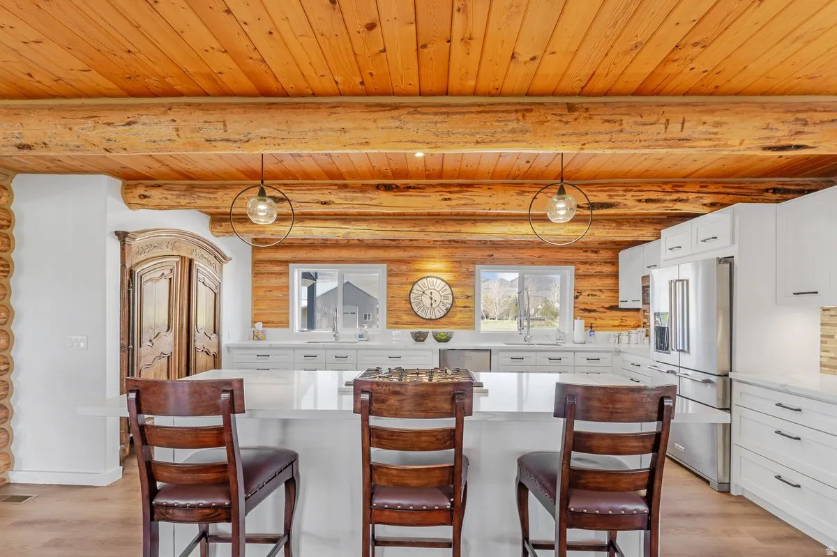 Kitchen with log wall accents, wood-finish flooring, white cabinetry, integrated stainless steel appliances, and a central island with countertop seating