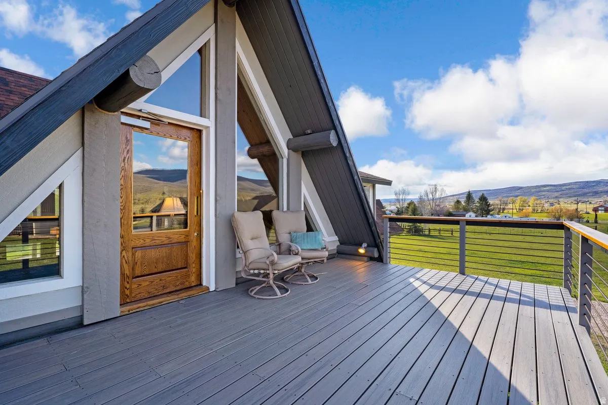 Expansive outdoor decking featuring a cable railing system, a wood-paneled entry door, A-frame architectural elements, and scenic surrounding topography