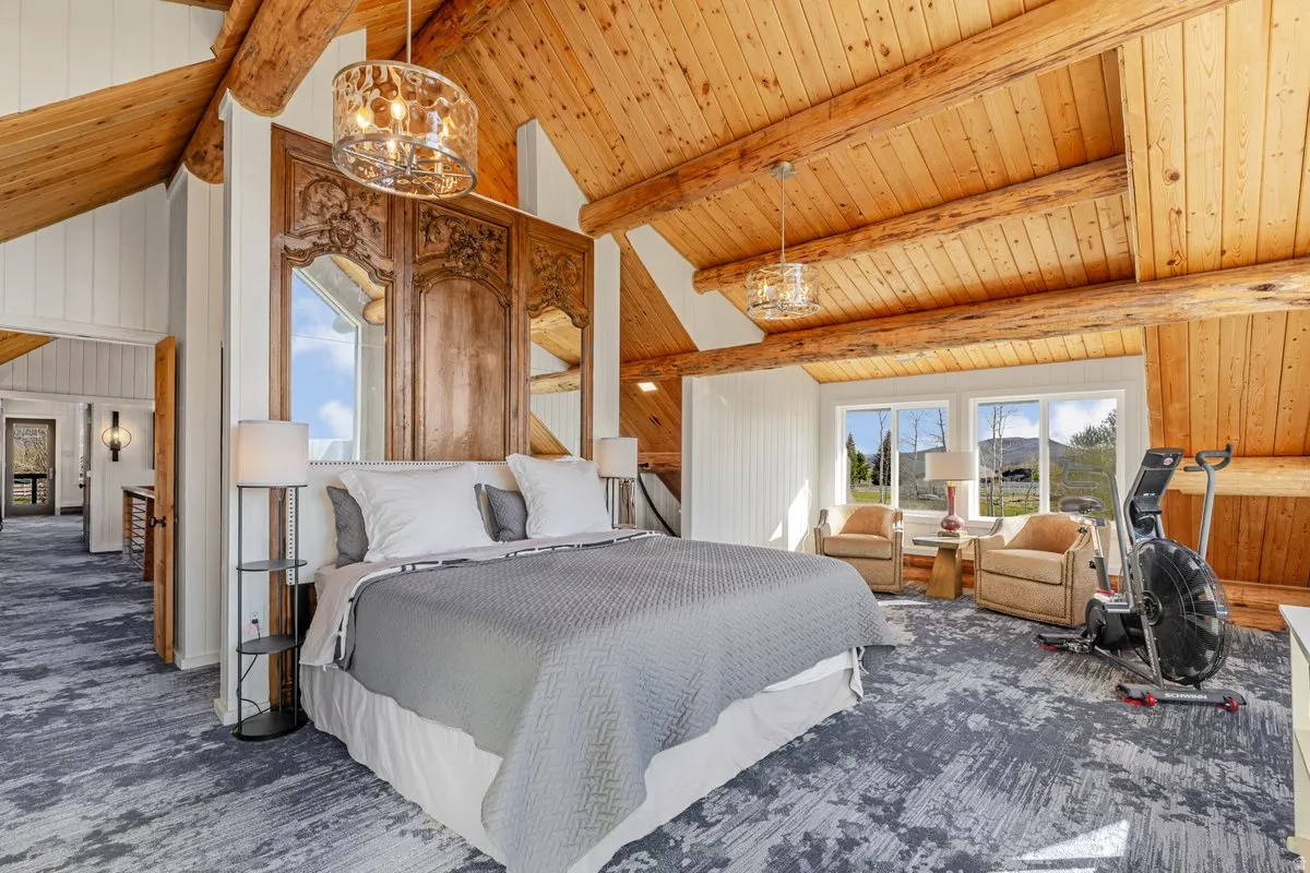 Vaulted wood-paneled ceilings with exposed log beams, two contemporary chandeliers, and a carved wood headboard with integrated mirrors