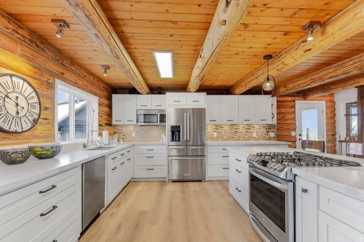 Spacious kitchen featuring white cabinetry, light-toned wood-finish flooring, stainless steel appliances, and a wood beam ceiling