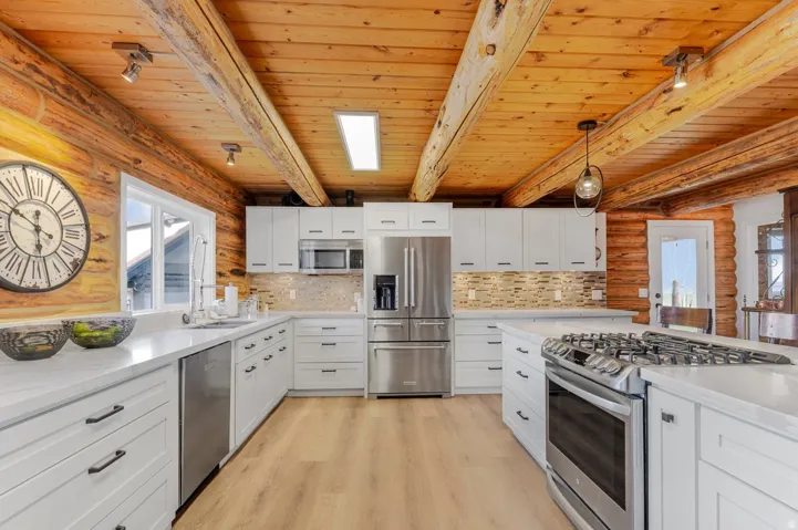 Spacious kitchen featuring white cabinetry, light-toned wood-finish flooring, stainless steel appliances, and a wood beam ceiling