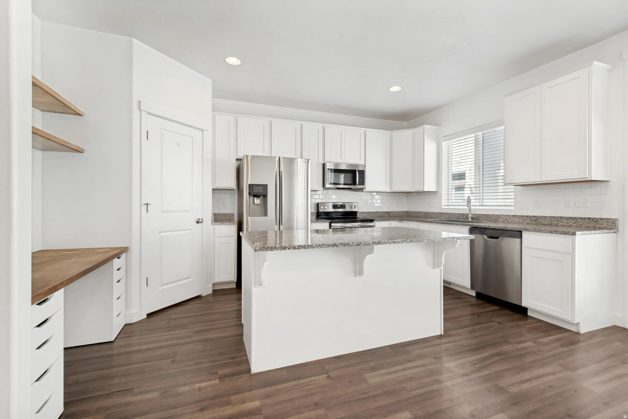 Bright kitchen featuring extensive white cabinetry, granite countertops, stainless steel appliances, a center island with additional storage, and wood-finish flooring