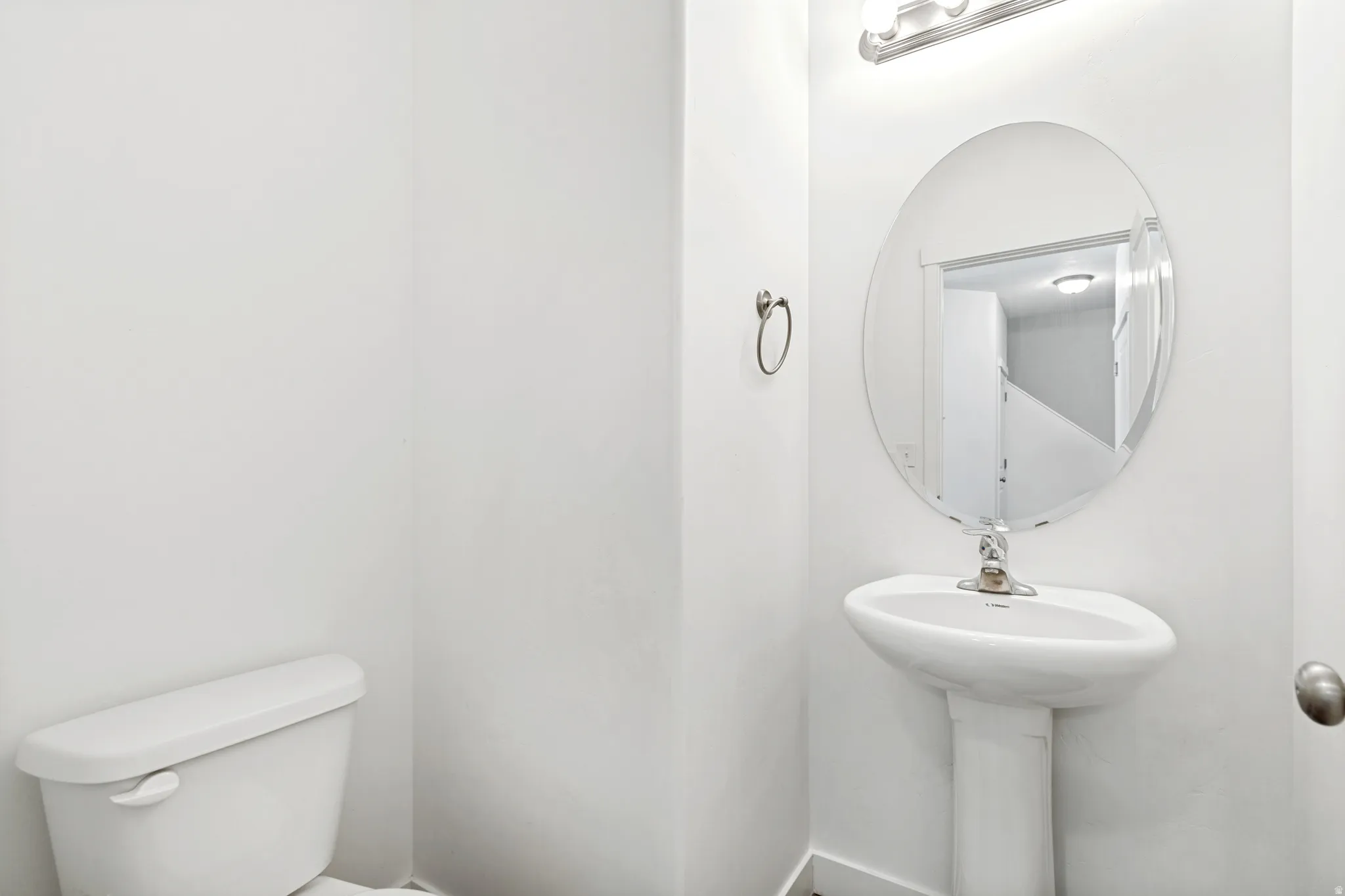 Pedestal sink with an oval frameless mirror and a wall-mounted light fixture