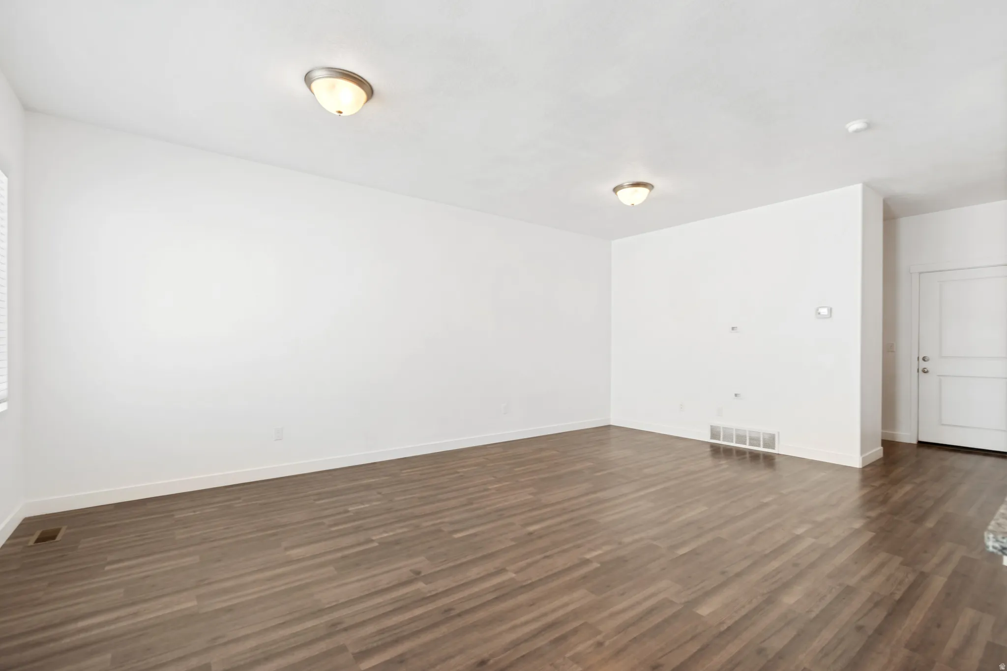 Spacious interior featuring wood-finish flooring, white walls, and flush-mount ceiling lights