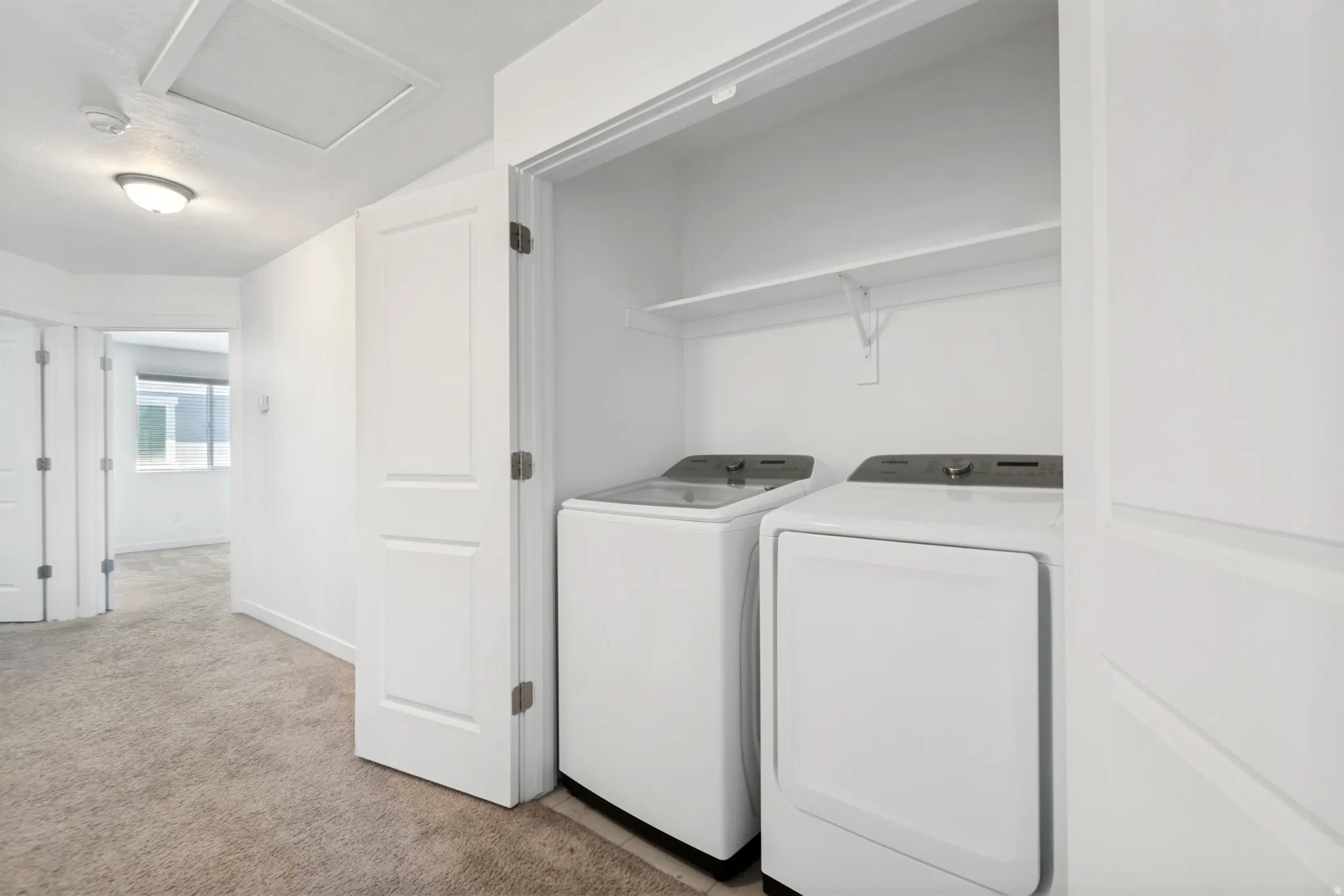 Dedicated laundry closet featuring a white shelf for storage and included white appliances