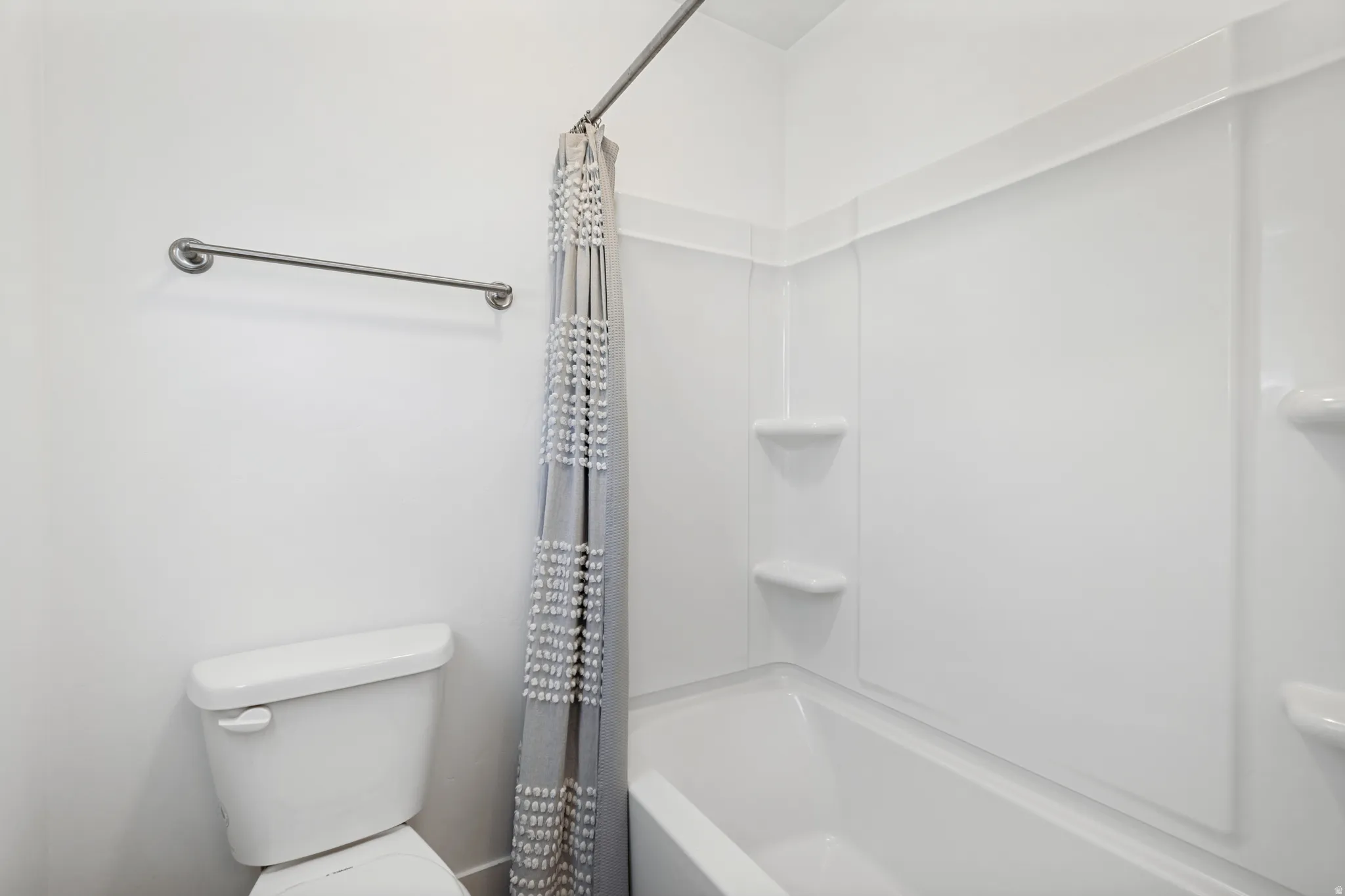Full-size bathtub with integrated shelving, a white toilet, and a wall-mounted towel bar
